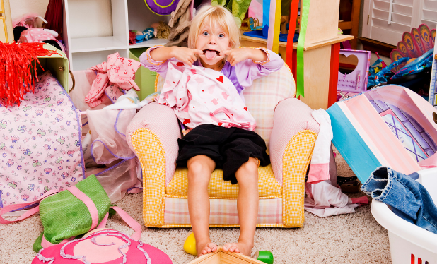 Child sitting in a chair in a messy Home Living Center, making silly face and sticking out tongue.